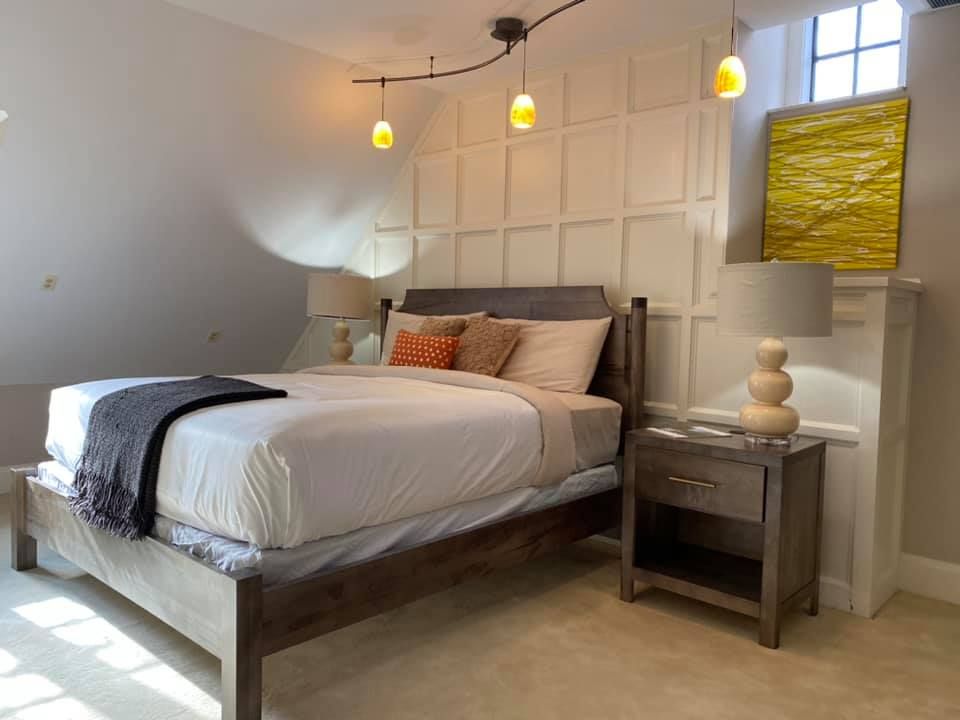 Modern guest bedroom with wooden bed frame, white paneled accent wall, track lighting