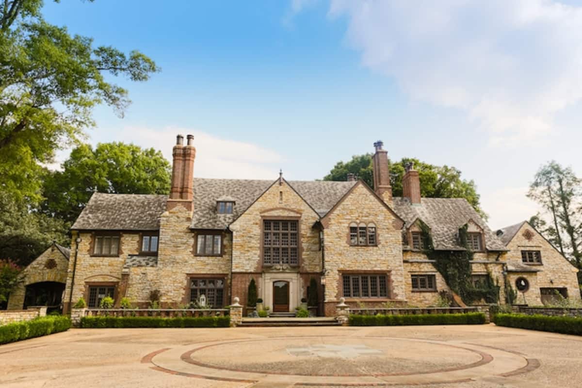 Stone mansion front facade with circular driveway and mature trees