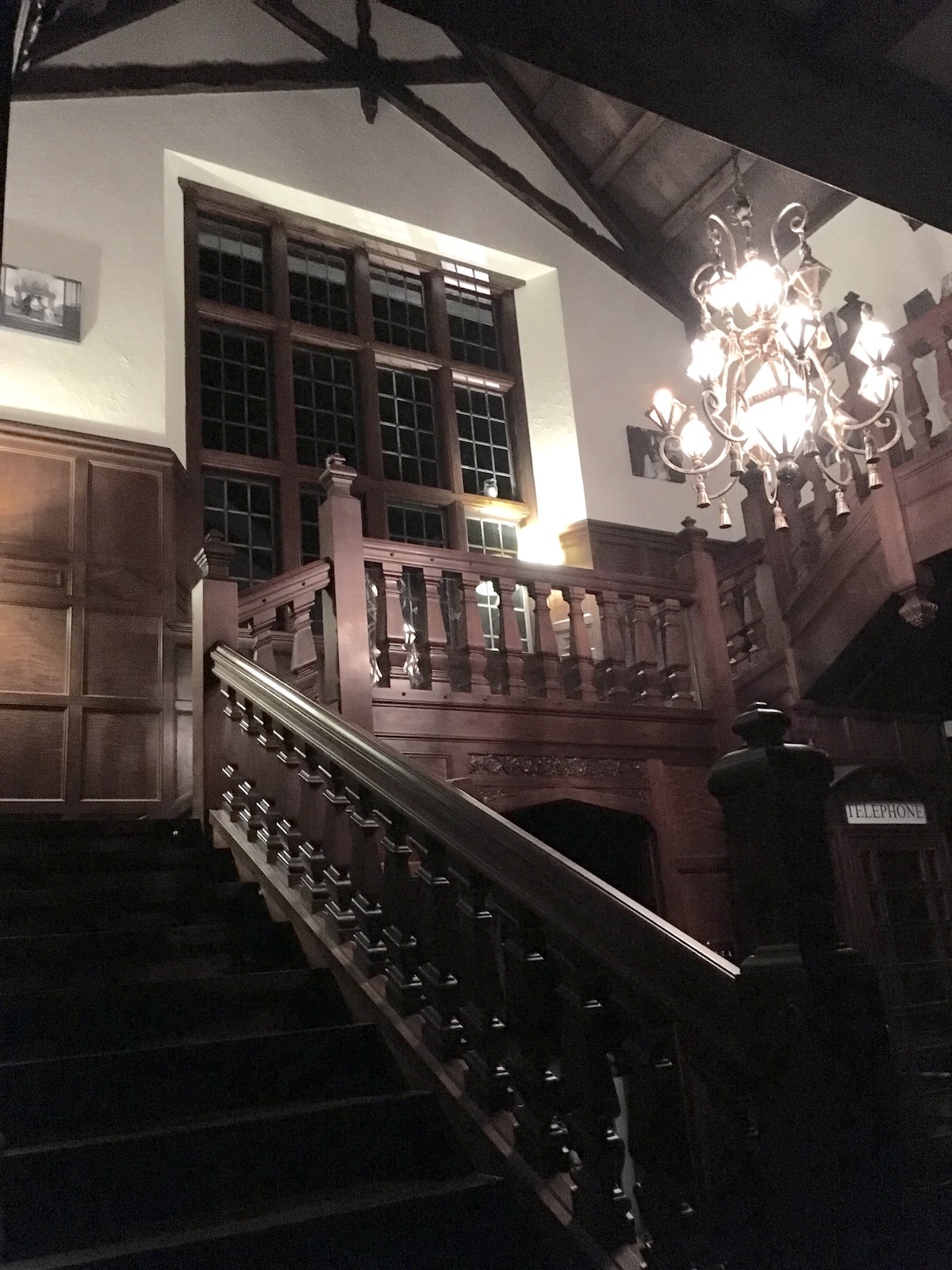 Grand dark wood staircase with chandelier and tall windows