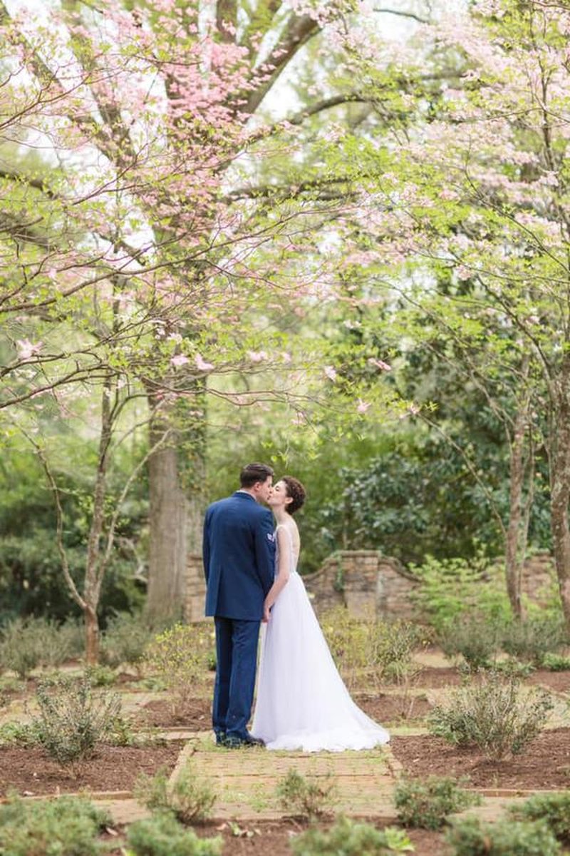 Bride and groom sharing a kiss on brick garden path beneath blooming pink dogwood trees