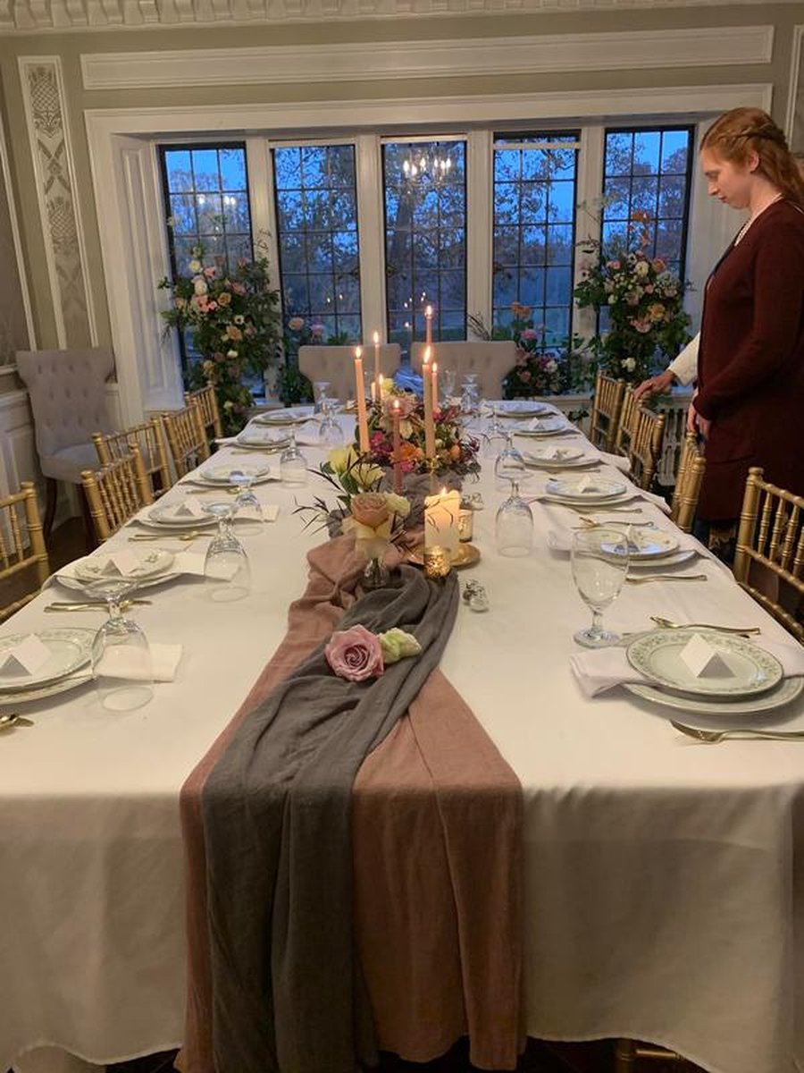 Formal dining table set for intimate reception with linen runners, taper candles, floral centerpieces, gold chiavari chairs