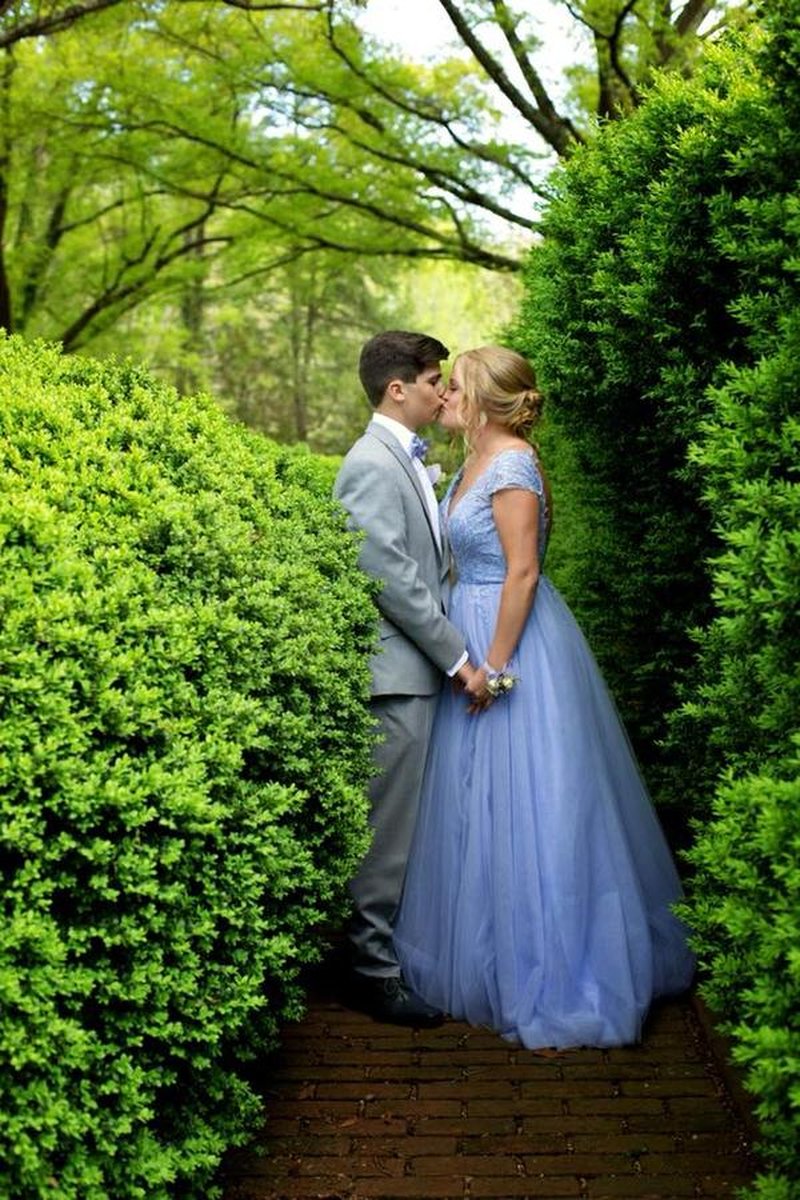 Couple sharing a kiss on brick pathway between sculpted hedges on estate grounds