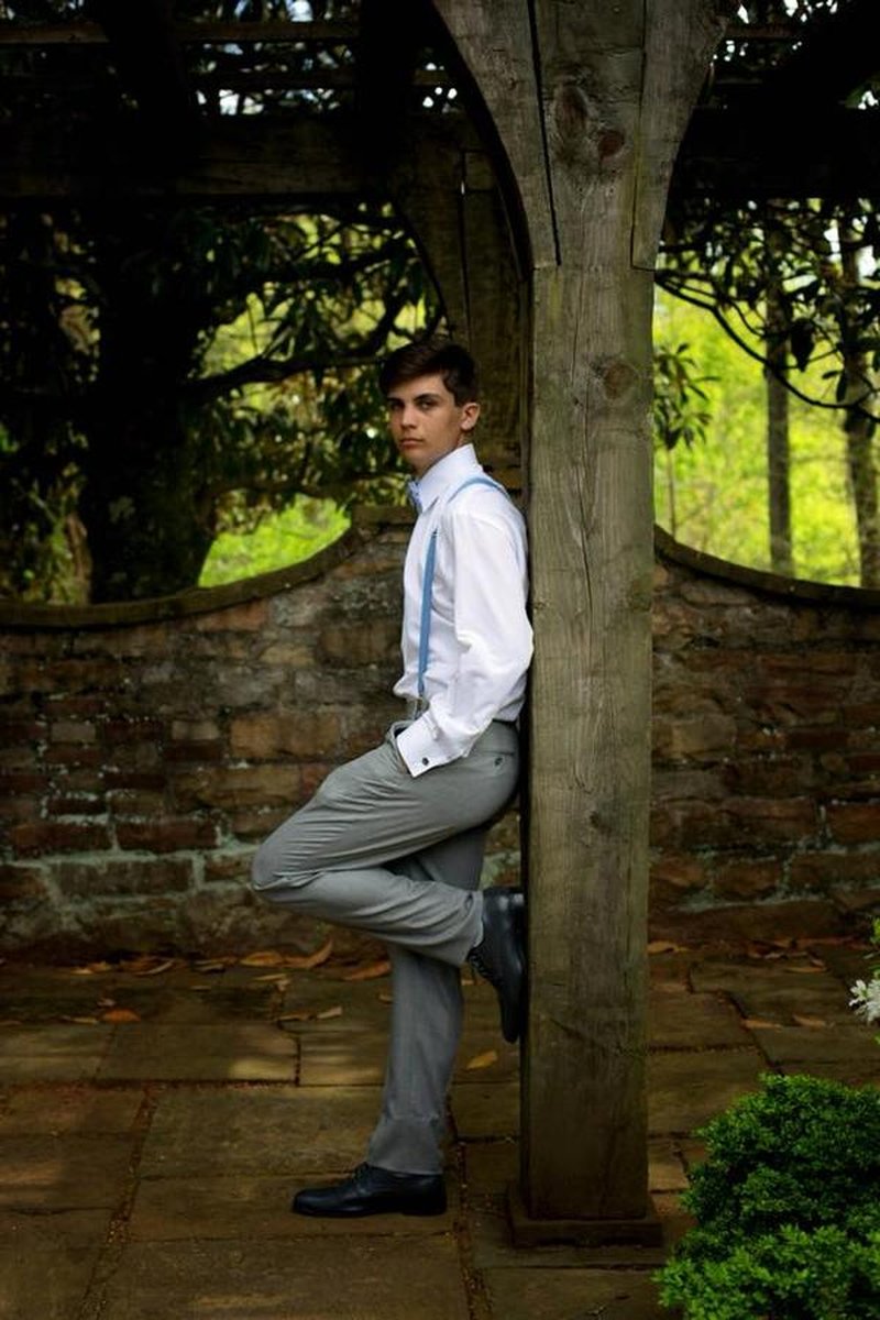 Young man in suspenders leaning against wooden pergola post in walled garden