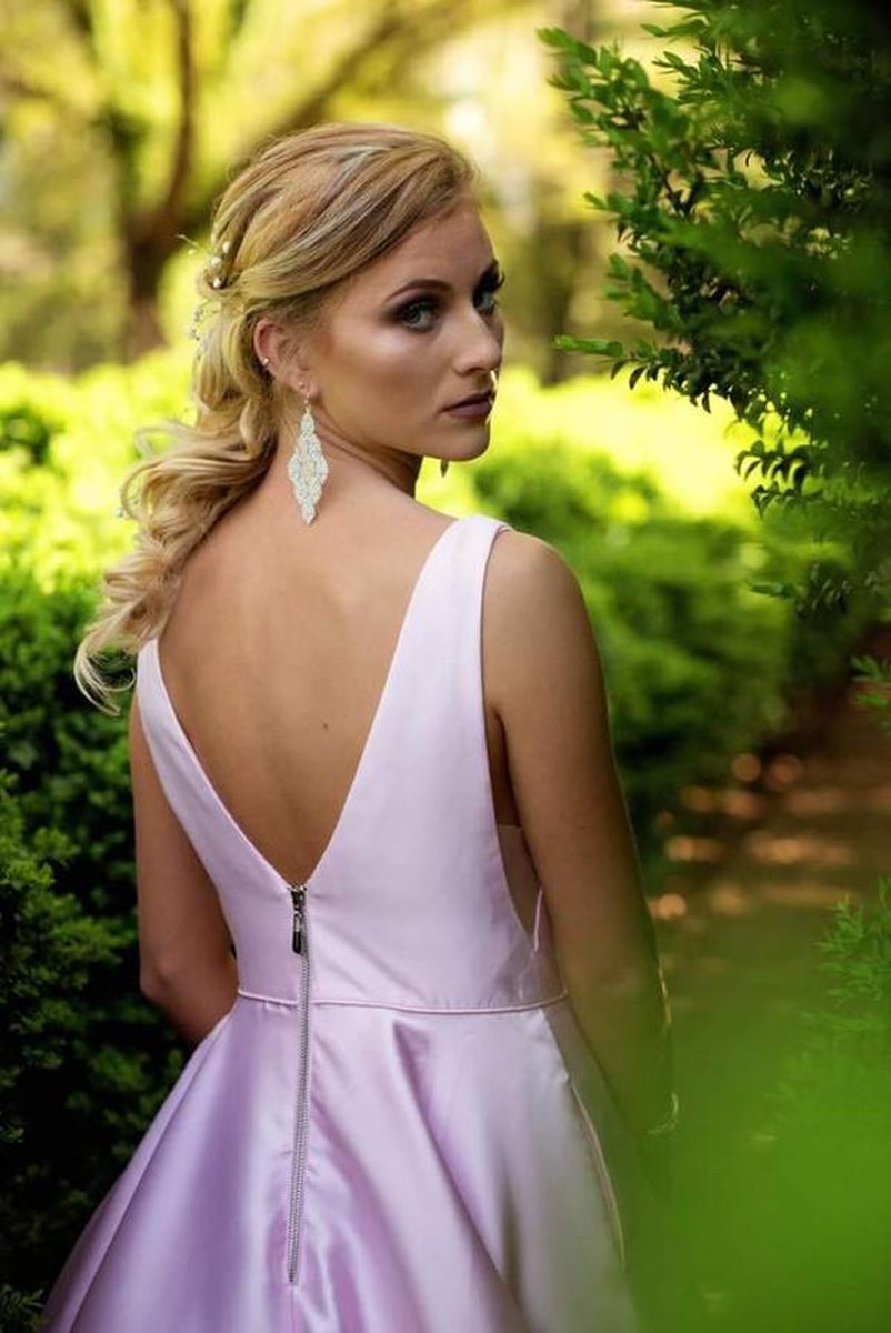 Close-up of woman showing back detail of low-cut satin dress, chandelier earrings among greenery