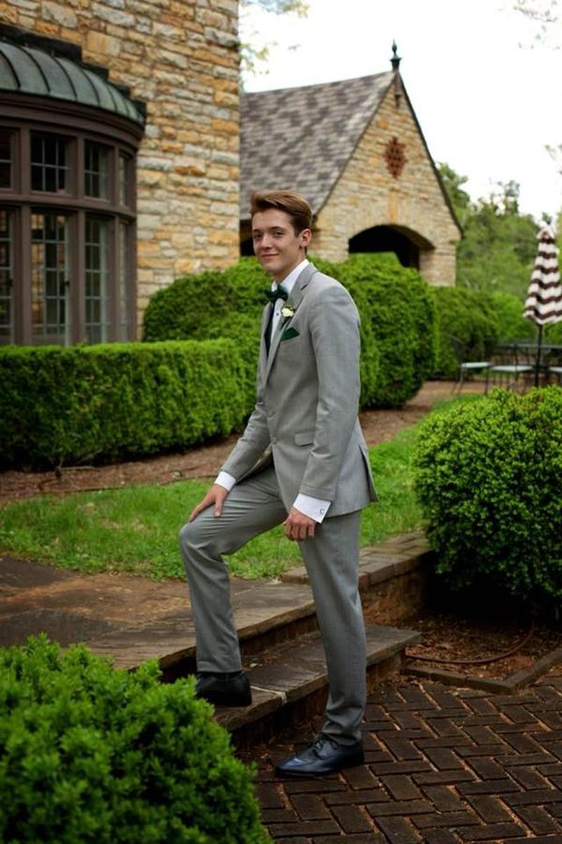 Young man in gray suit with bow tie posing on stone steps with mansion and hedges behind
