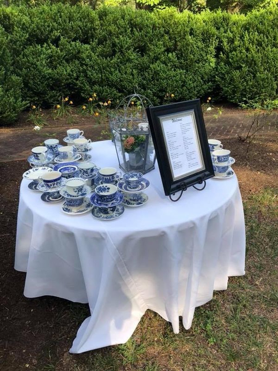 Round accent table displaying blue-and-white teacups, glass terrarium, and framed welcome menu
