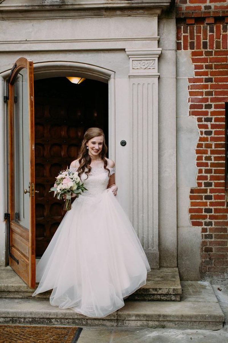 Bride emerging from ornate mansion doorway with brick and stone facade