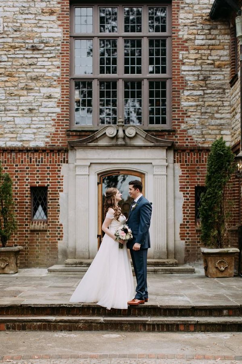 Bride and groom gazing at each other on stone steps in front of Tudor-style mansion entrance