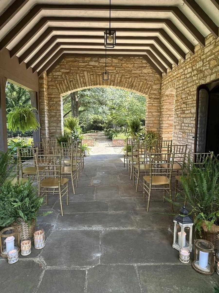Intimate ceremony setup under stone archway with gold chiavari chairs, lanterns, and ferns