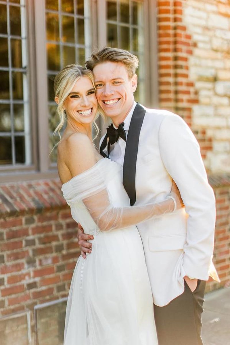 Bride and groom smiling and embracing in golden hour light in front of brick mansion