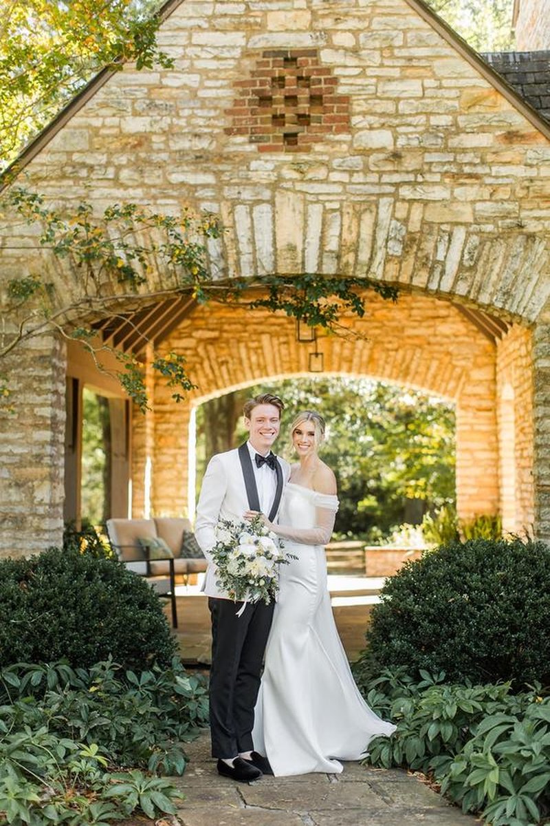 Bride and groom posing together under stone archway of mansion