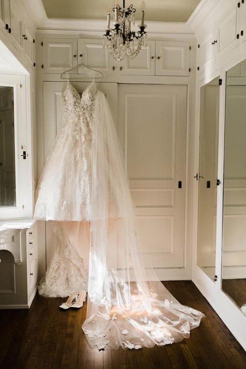 Wedding dress and veil hanging from chandelier in elegant white-paneled dressing room