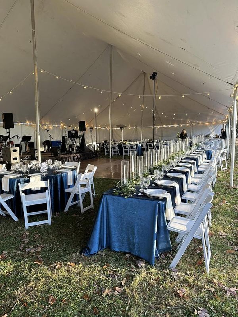 Tented wedding reception with long banquet tables, navy blue linens, string lights, band setup, dance floor