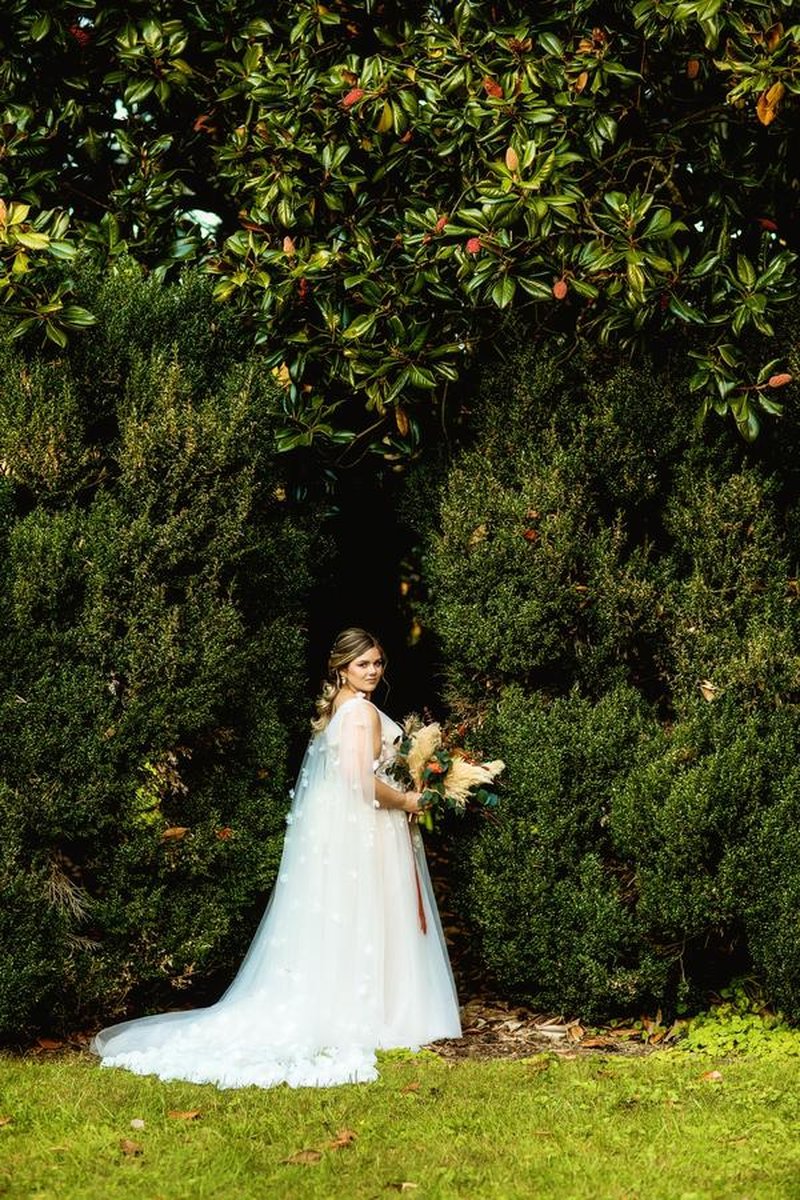 Bride posing with bouquet of pampas grass and autumn flowers in front of boxwood hedges
