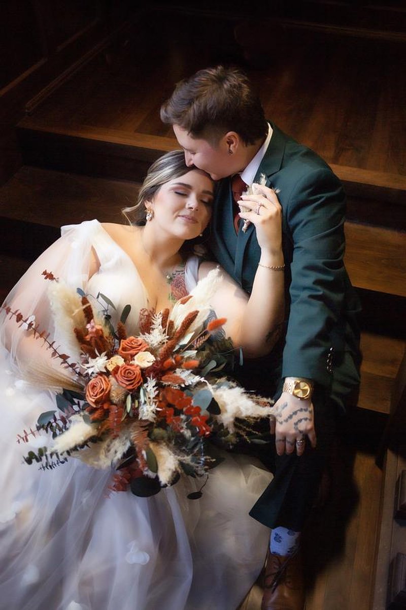 Intimate couple portrait on wooden staircase with autumn-toned bouquet, shot from above