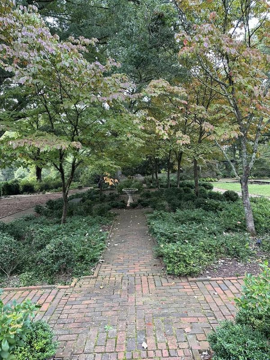 Brick pathway through shaded garden with autumn foliage, ground cover, and birdbath