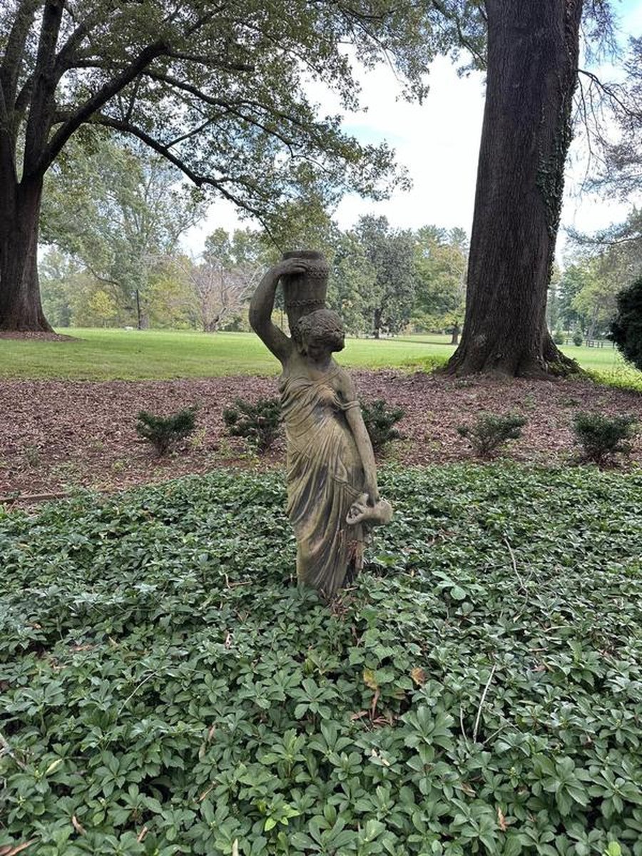 Classical stone statue of draped female figure among pachysandra with expansive lawn