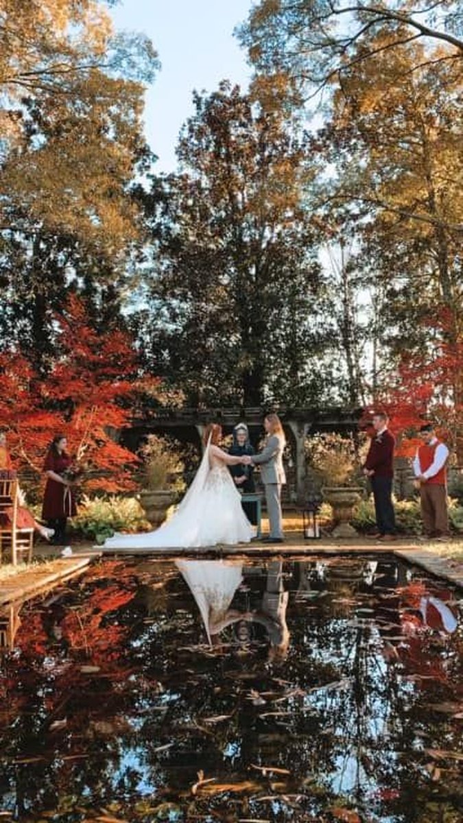 Autumn wedding ceremony by reflecting pool surrounded by vibrant red and orange foliage
