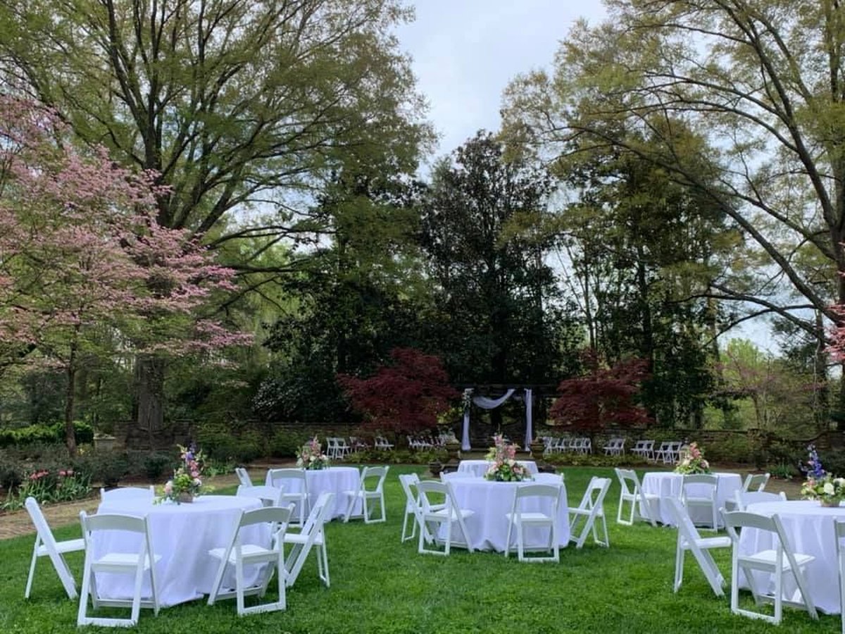 Outdoor wedding reception on lush green lawn with white round tables, folding chairs, and blooming dogwood trees