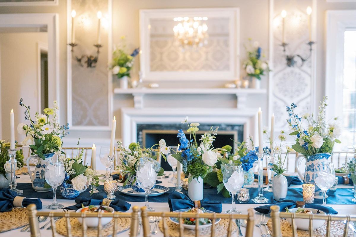Full tablescape in mansion dining room with blue runner, floral arrangements, gold chiavari chairs, fireplace mantel