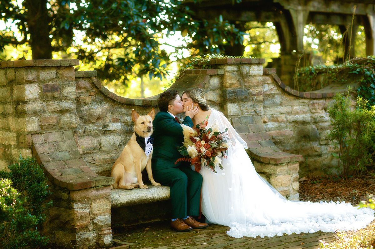 Couple kissing on stone bench in garden with dog in tuxedo bib, autumn bouquet