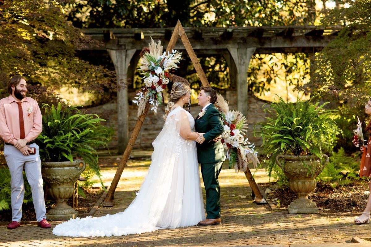 Outdoor wedding ceremony under triangular wooden arch with boho florals and pampas grass